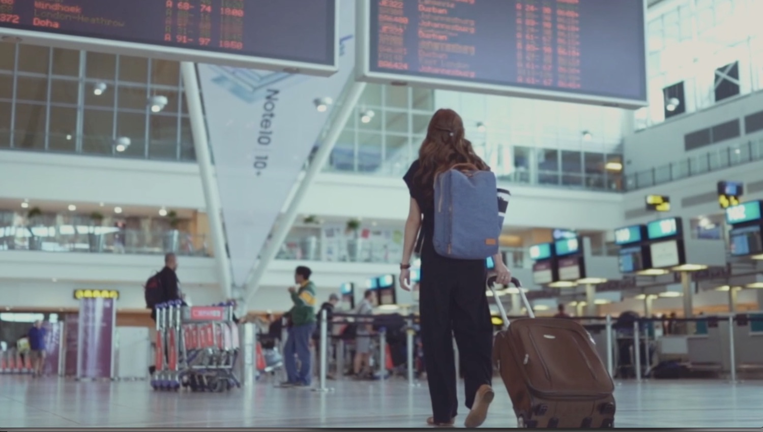 A traveler walking through an airport terminal beneath departure boards.