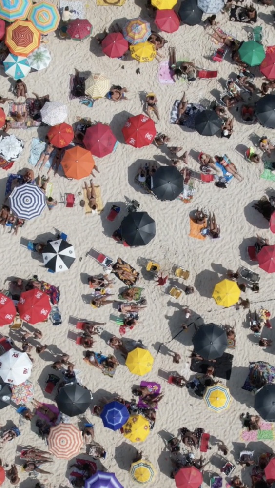 Aerial drone shot of a crowded beach patterned with colorful umbrellas.